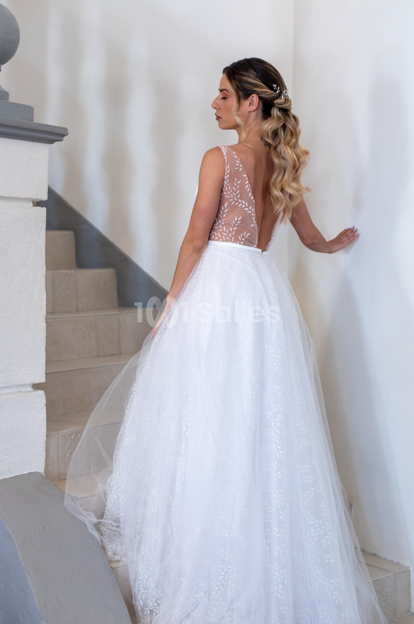 Femme en robe de mariée blanche avec dos en dentelle transparente, montant un escalier intérieur en pierre.