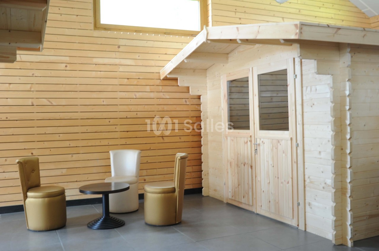 Cabine en bois dans un intérieur avec murs en lambris, accompagnée de deux fauteuils et une table basse.