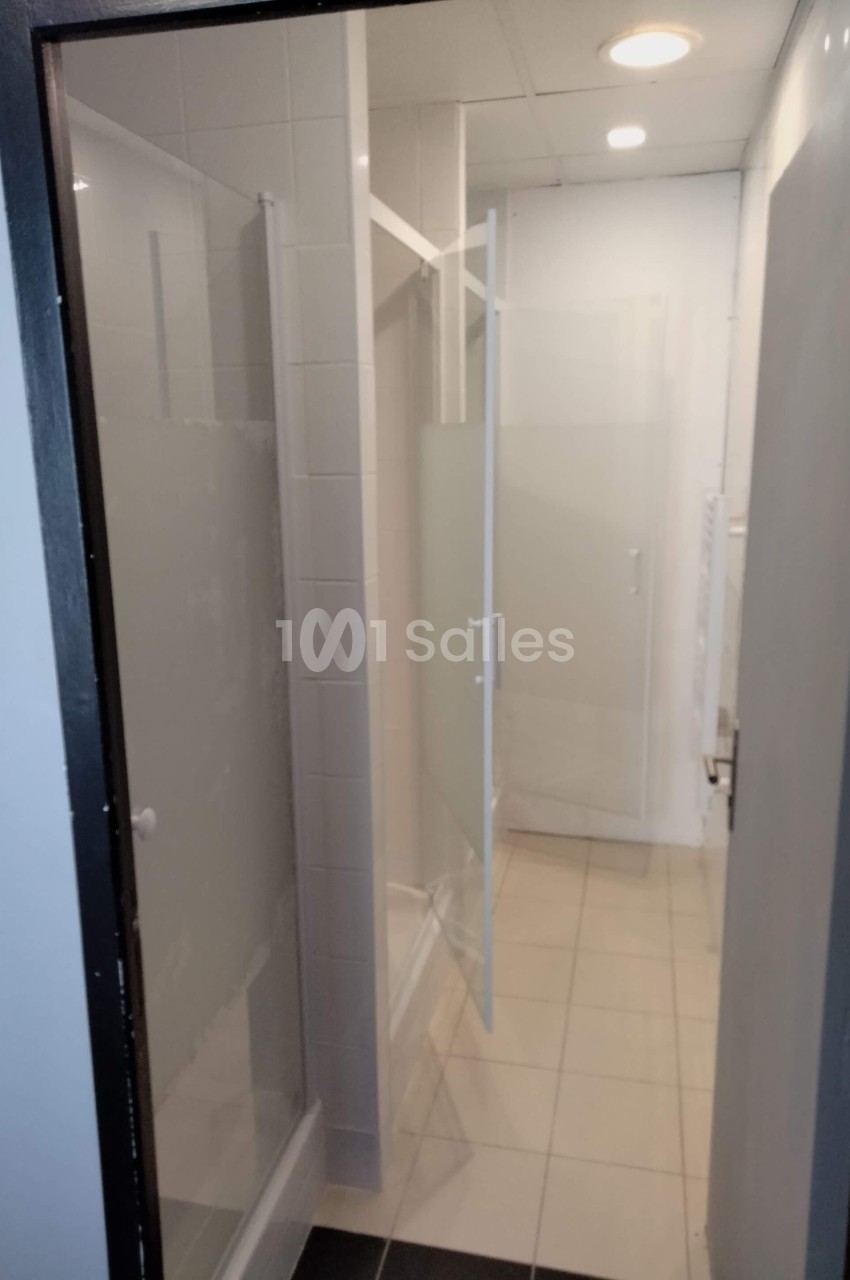 Cabines de douche avec parois vitrées dépolies dans un couloir carrelé éclairé par des spots au plafond.