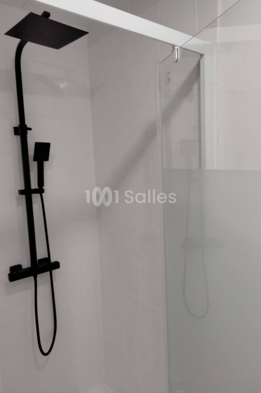 Douche moderne avec paroi vitrée partiellement opaque et colonne de douche noire fixée au mur blanc.