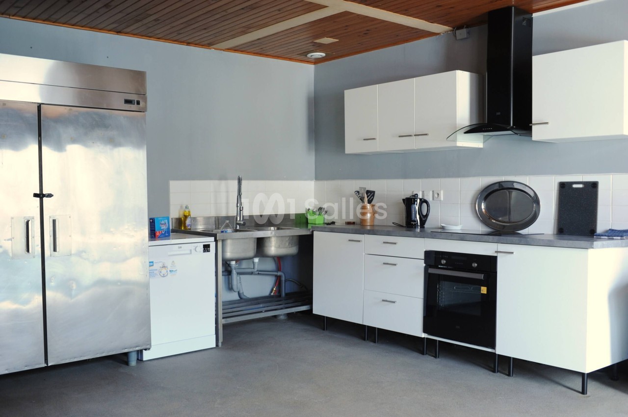 Cuisine moderne avec réfrigérateur en acier inoxydable, évier double, plaques de cuisson, four et rangements blancs.