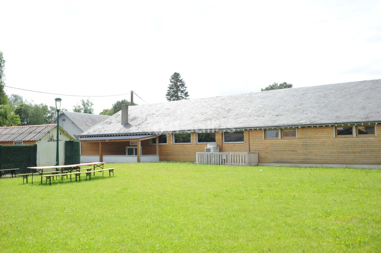 Bâtiment en bois avec toit en ardoise, entouré d'une pelouse, tables de pique-nique au premier plan.