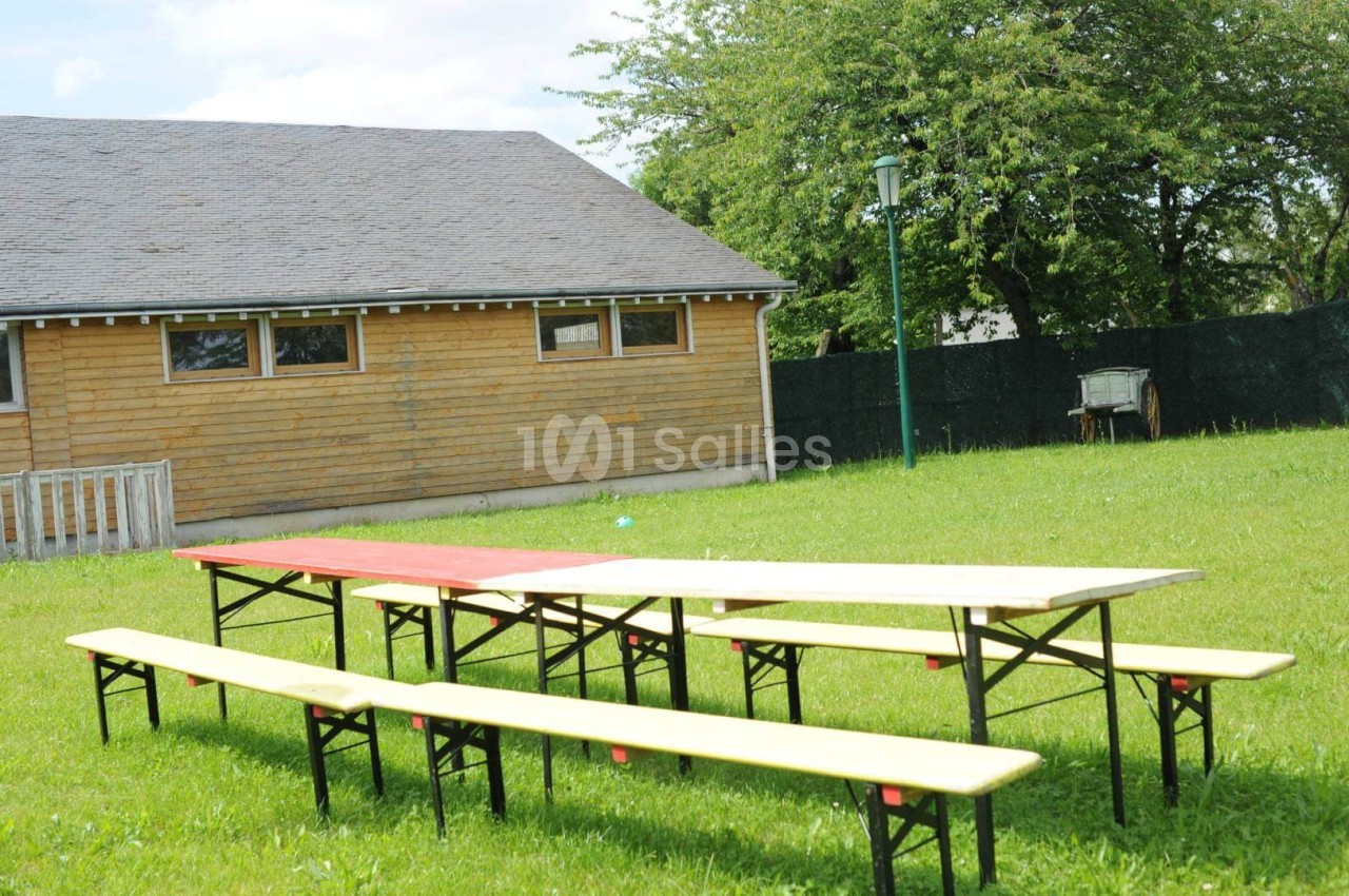 Tables et bancs en bois disposés sur une pelouse, près d'un bâtiment en bois et d'arbres en arrière-plan.