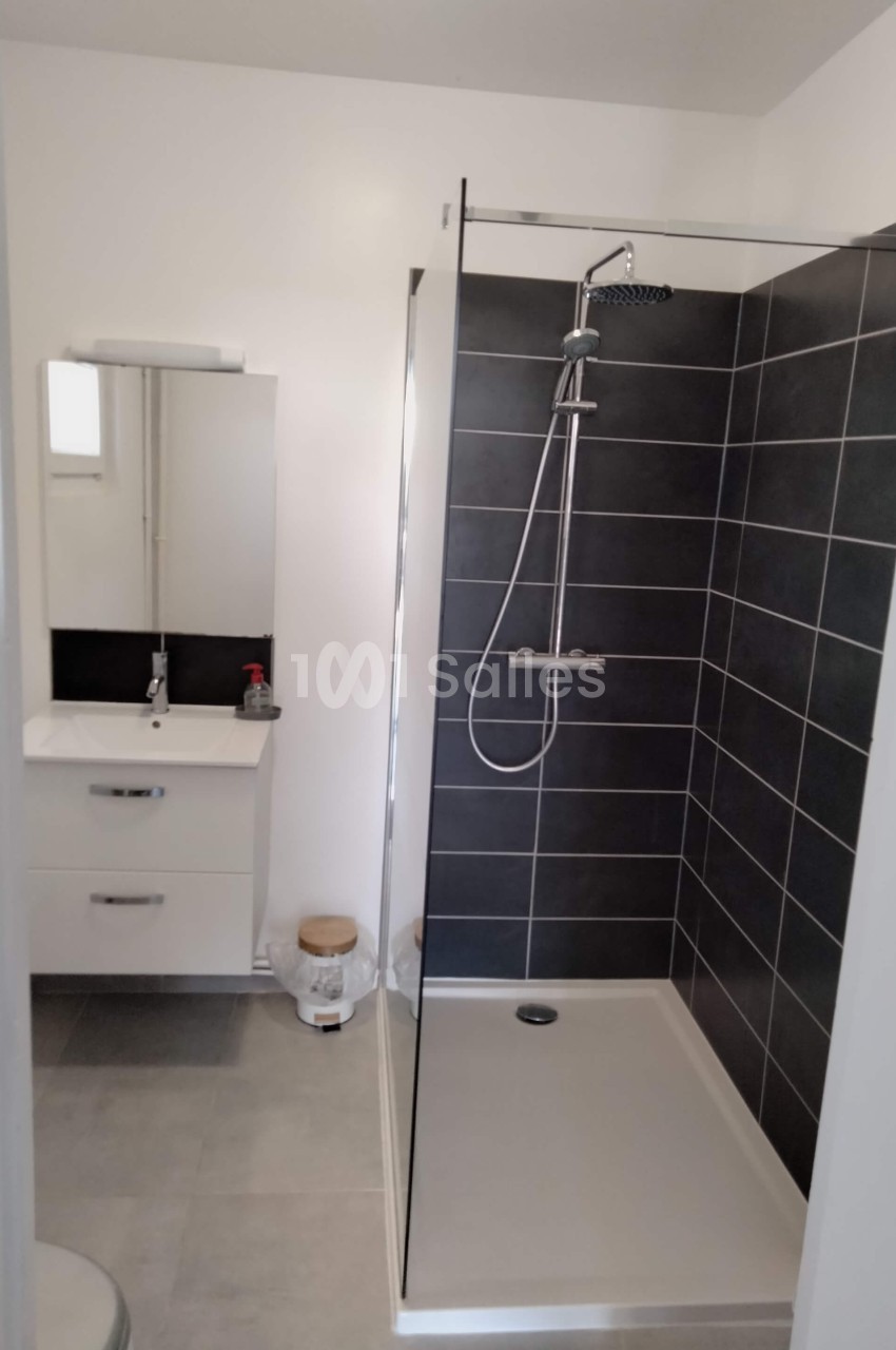 Salle de bain moderne avec douche à l'italienne, carrelage noir, meuble lavabo blanc et miroir éclairé.