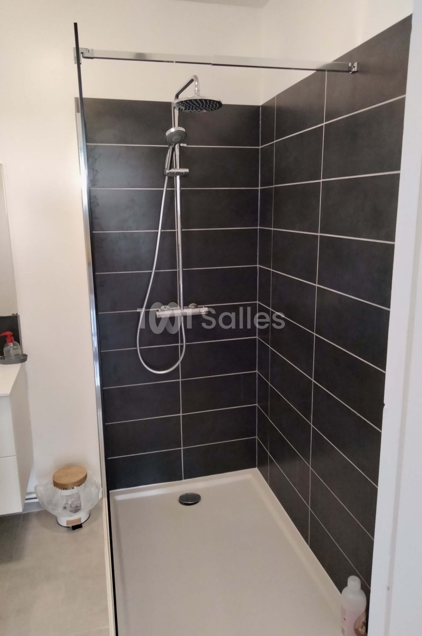 Douche moderne avec paroi vitrée, carrelage noir, pommeau de douche et mitigeur, située dans une salle de bain lumineuse.