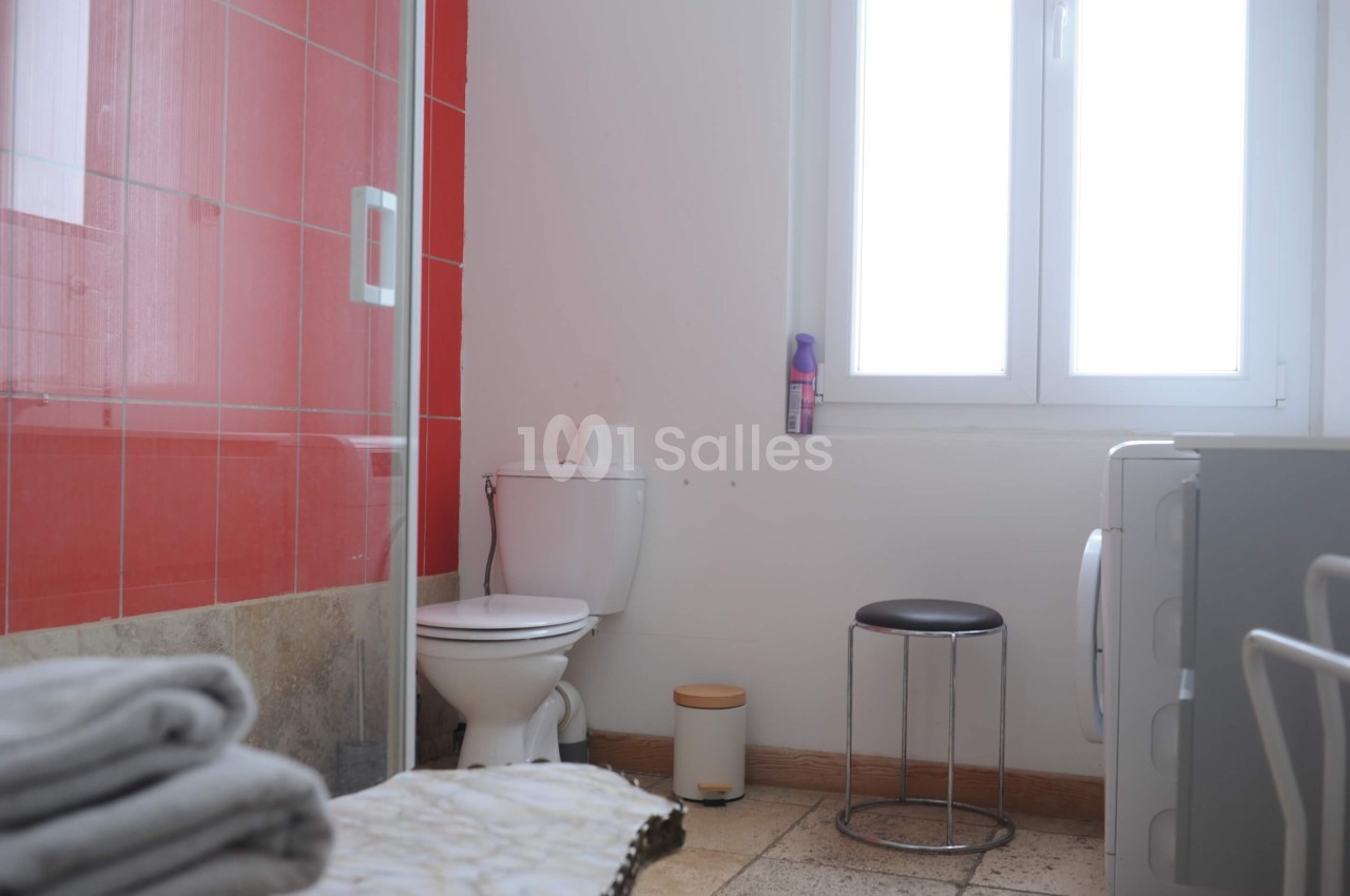 Salle de bain lumineuse avec toilettes, douche à paroi rouge, fenêtre, tabouret et machine à laver.
