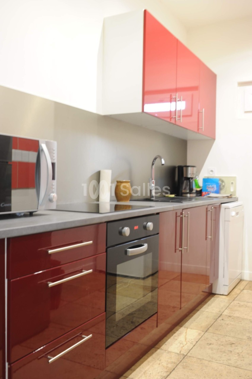 Cuisine moderne avec meubles rouges brillants, four encastré, micro-ondes, évier, cafetière et lave-vaisselle.