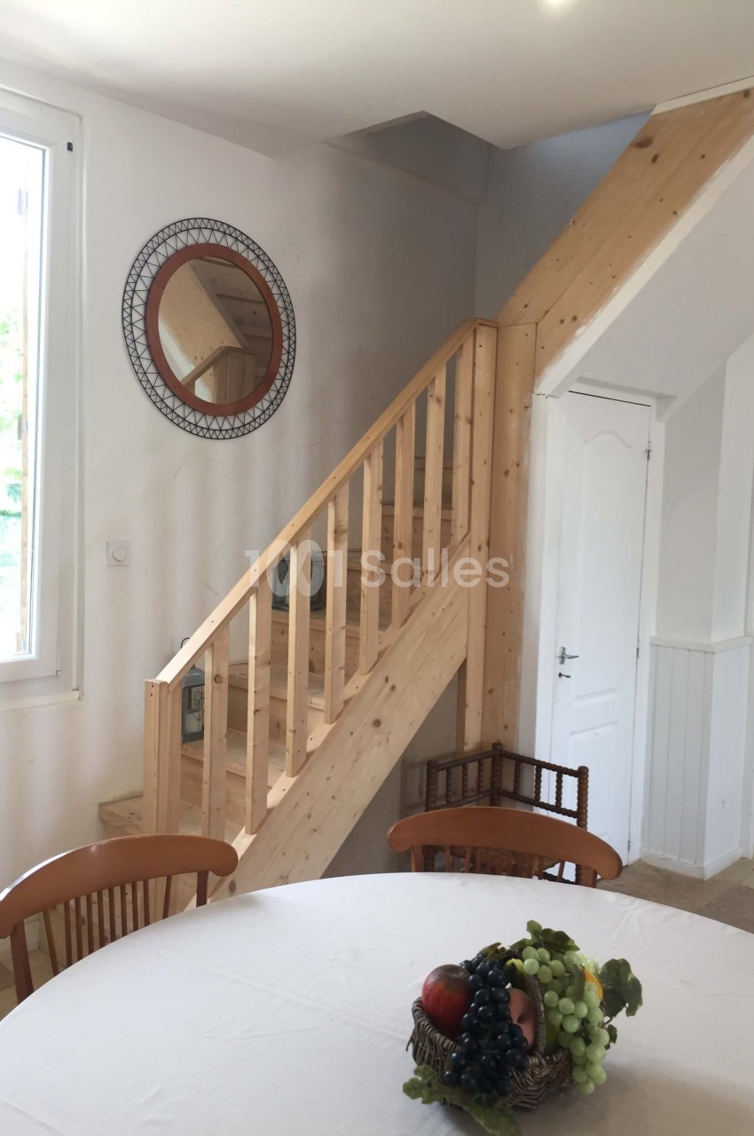 Escalier en bois clair dans un intérieur lumineux, avec une table ronde et un miroir mural circulaire.