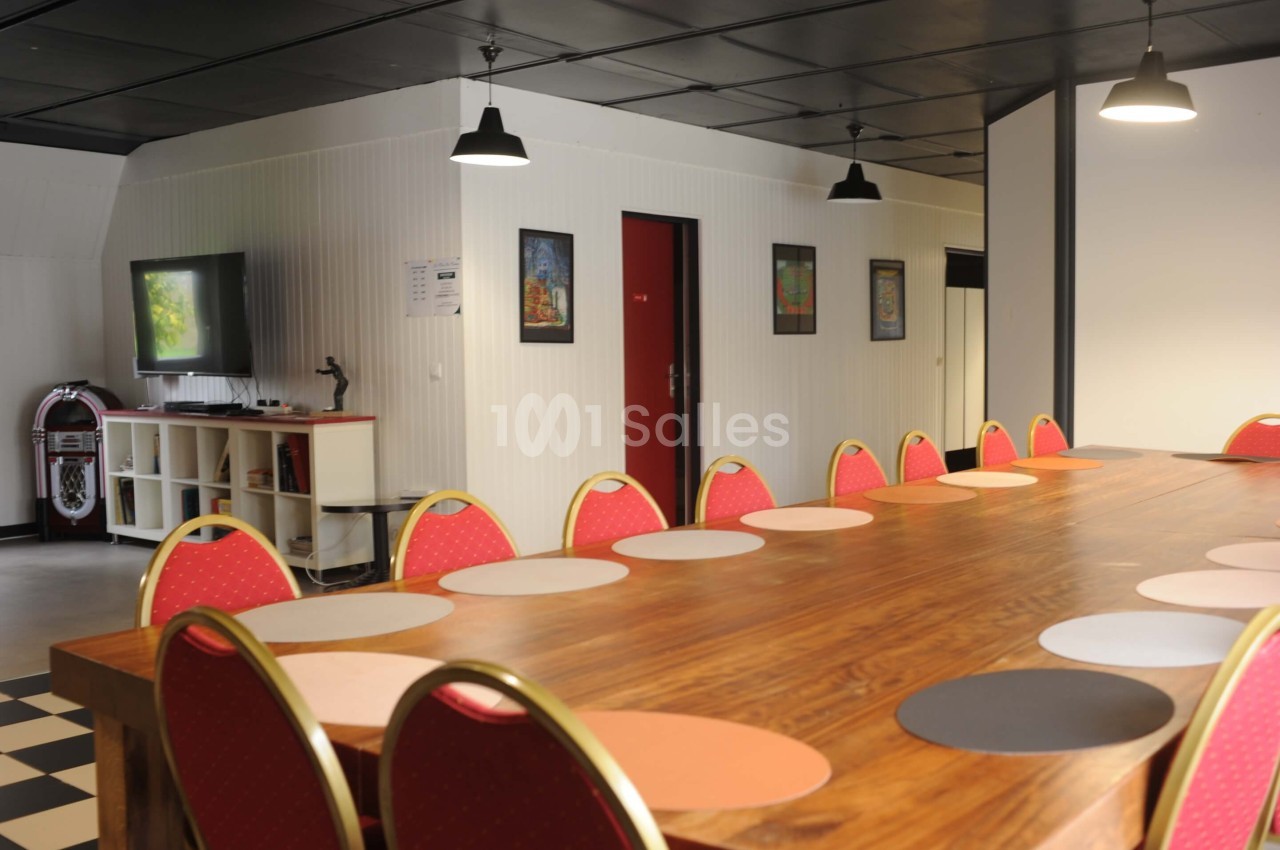 Grande table en bois entourée de chaises rouges dans une salle lumineuse avec décorations murales et éclairage suspendu.