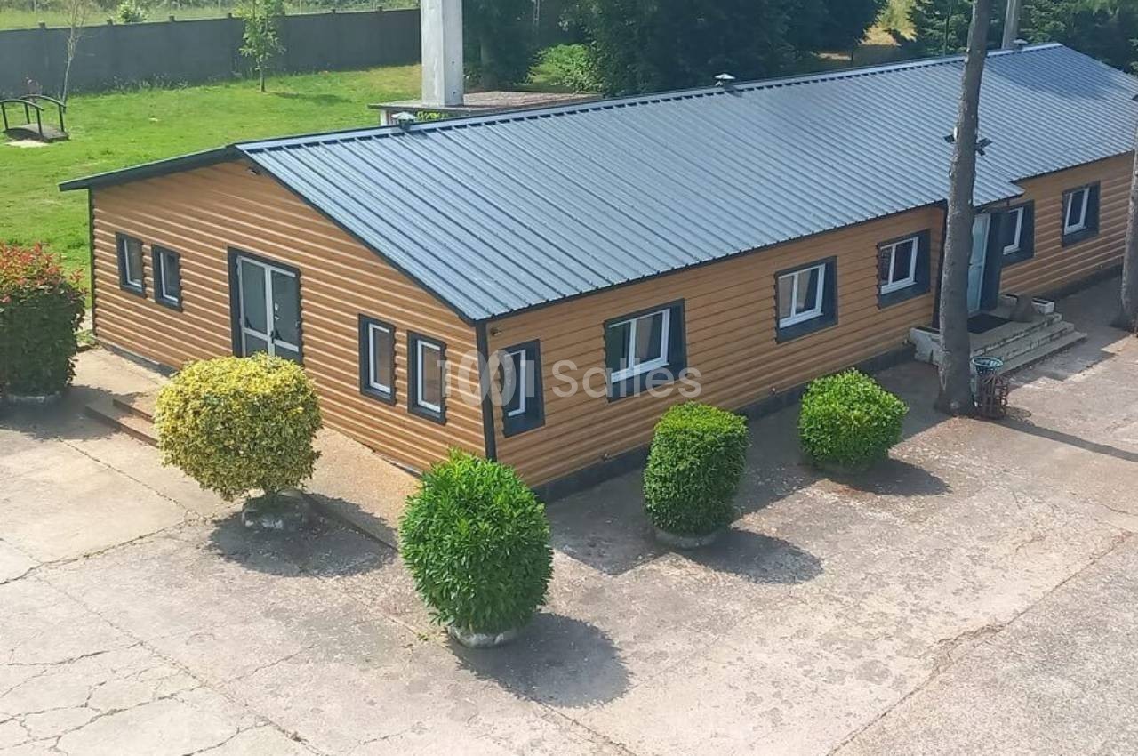 Bâtiment en bois avec toit en tôle, entouré de buissons taillés, situé dans une cour pavée.