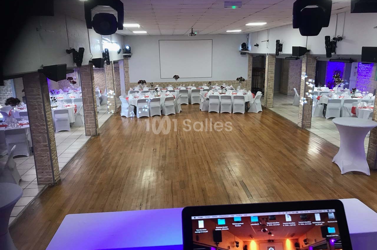 Salle de réception spacieuse avec parquet, tables dressées pour un événement et écran de projection en fond.
