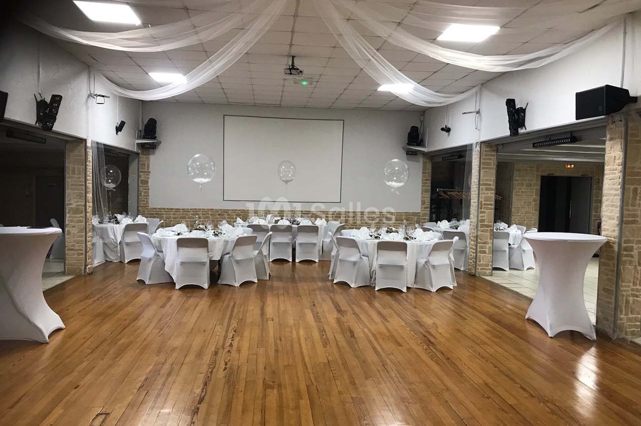 Salle de réception avec tables rondes dressées, nappes blanches et décoration sobre sous un plafond voilé.