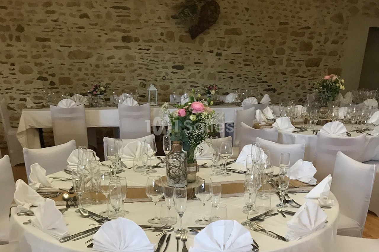 Salle de réception décorée avec des tables rondes dressées, nappes blanches et centres de table fleuris.