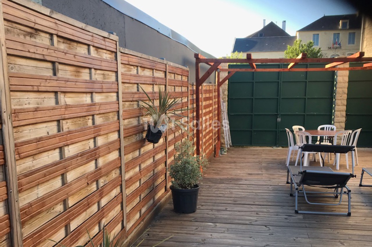 Terrasse en bois avec clôture en lattes, pergola, mobilier de jardin et plantes en pots.