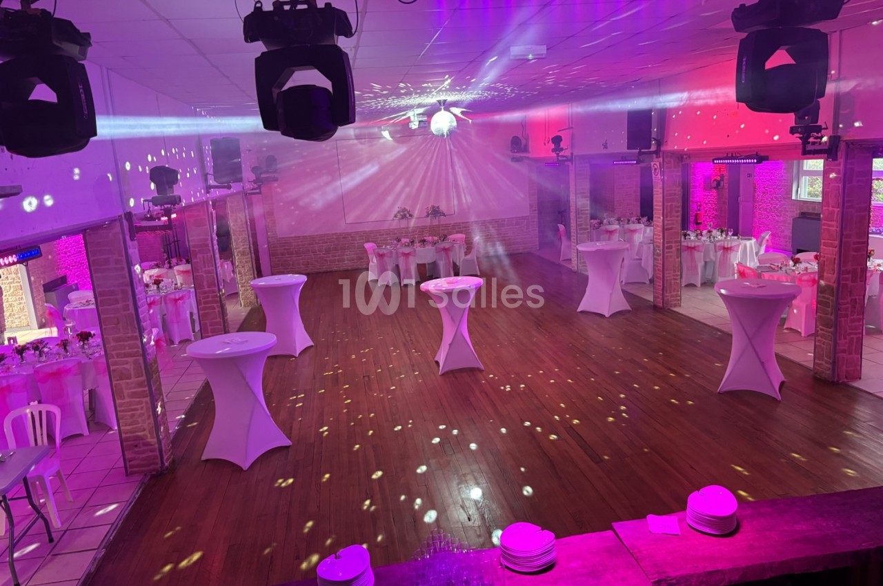 Salle de réception décorée avec des tables hautes et des jeux de lumière, prête pour un événement festif.