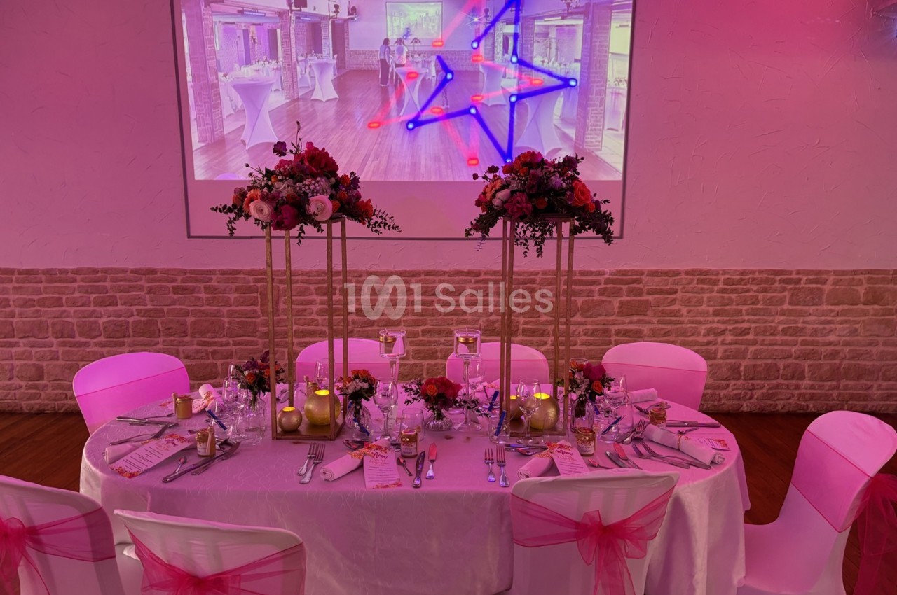 Table décorée pour un événement avec nappes blanches, chaises ornées de rubans roses et centre de table floral.