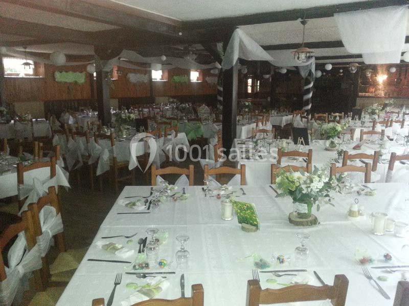 Salle de réception décorée avec des tables dressées pour un événement, ornées de nappes blanches et de compositions florales.