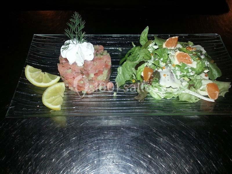 Assiette composée d'un tartare de poisson garni de crème et d'aneth, accompagnée d'une salade verte et de quartiers de…