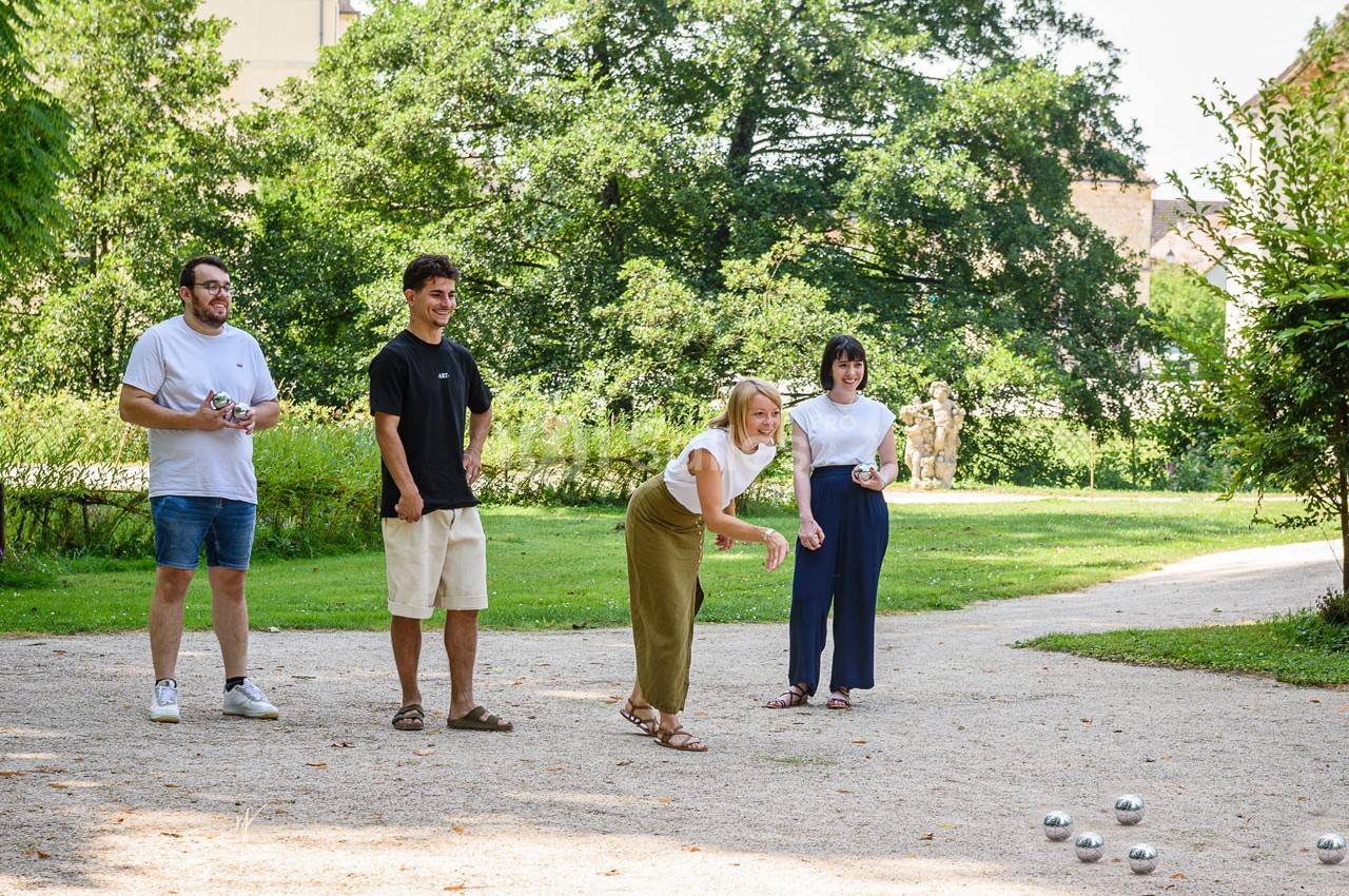 Quatre personnes jouent à la pétanque dans un parc verdoyant par une journée ensoleillée.