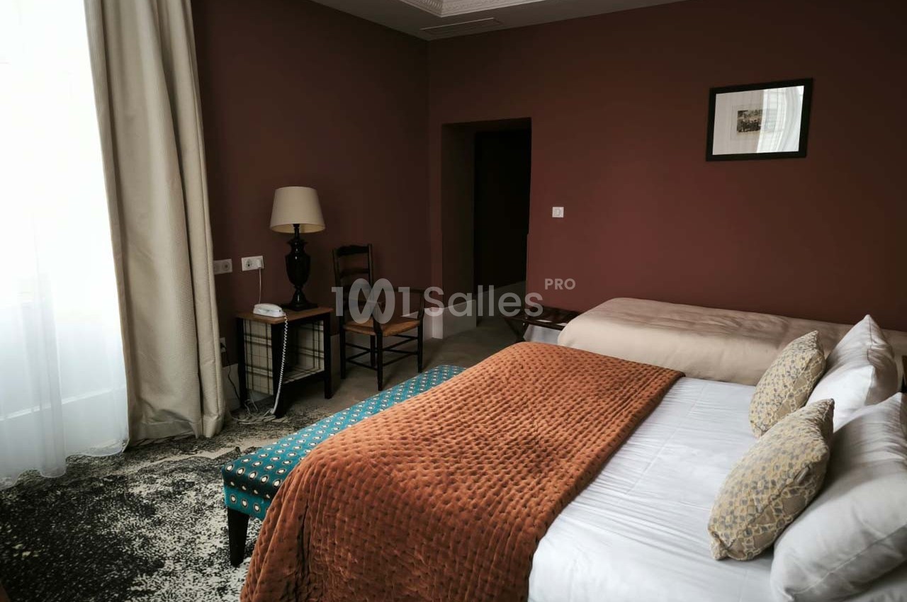 Chambre avec deux lits, murs couleur terracotta, rideaux clairs, tapis au sol et mobilier en bois sombre.