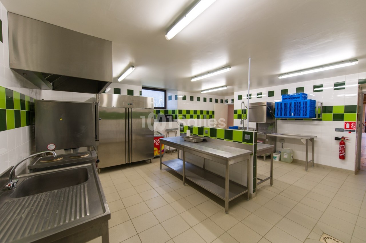 Cuisine professionnelle avec équipements en inox, carrelage blanc et vert, éclairage fluorescent et espace de travail…