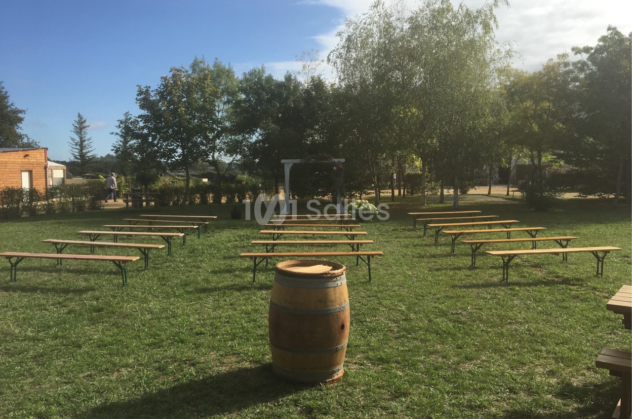Alignement de bancs en bois sur une pelouse, avec un tonneau au premier plan et des arbres en arrière-plan.