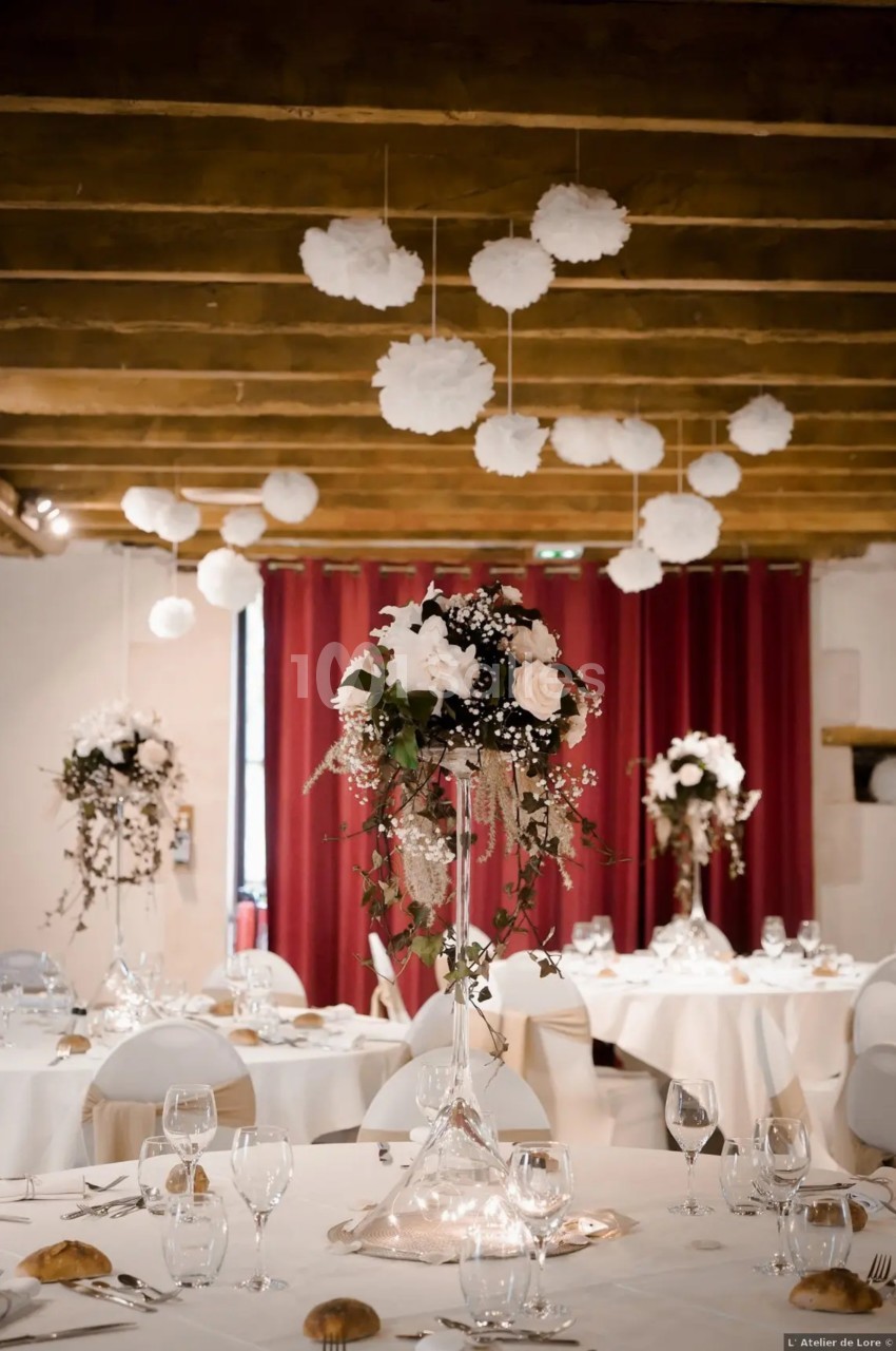 Salle de réception décorée avec des tables élégantes, centres de table floraux et suspensions blanches au plafond.