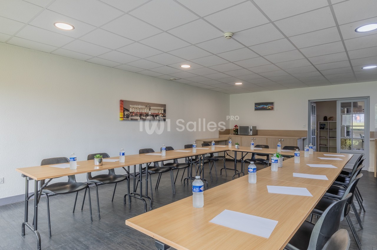 Salle de réunion lumineuse avec tables disposées en U, chaises, bouteilles d'eau et feuilles de papier sur les tables.