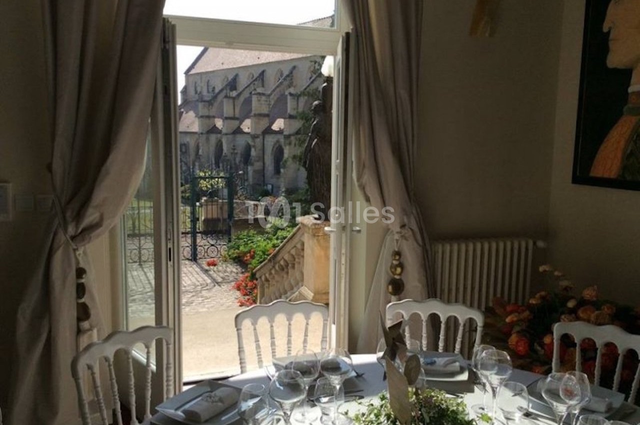 Salle à manger élégante avec table dressée, donnant sur une terrasse et une vue sur un bâtiment ancien.