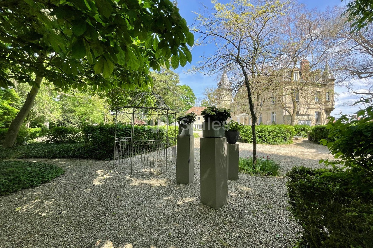 Allée gravillonnée bordée de verdure, avec des colonnes décoratives et un bâtiment ancien en arrière-plan.