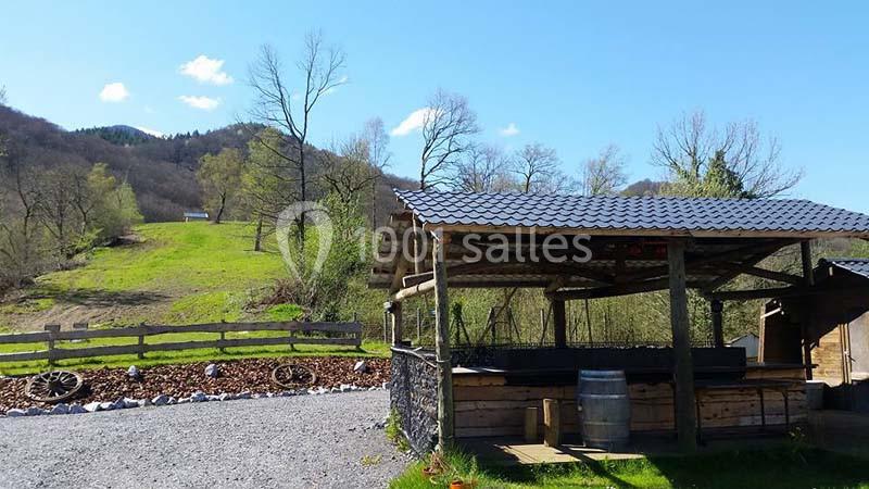 Abri en bois avec toit en tôle, entouré de nature verdoyante et collines sous un ciel bleu clair.