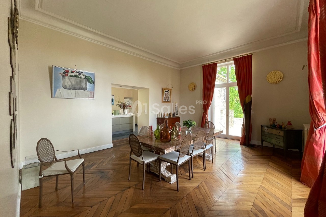 Salle à manger lumineuse avec table en verre, chaises en osier, parquet en bois et grandes fenêtres donnant sur un jardin.