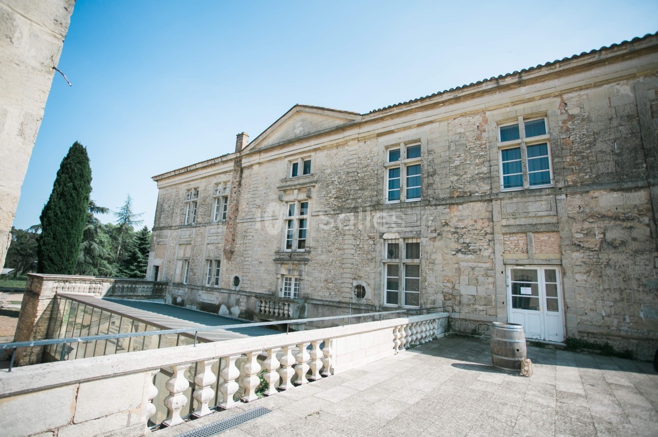 Façade en pierre d'un bâtiment ancien avec balustrade, fenêtres à carreaux et ciel dégagé en arrière-plan.