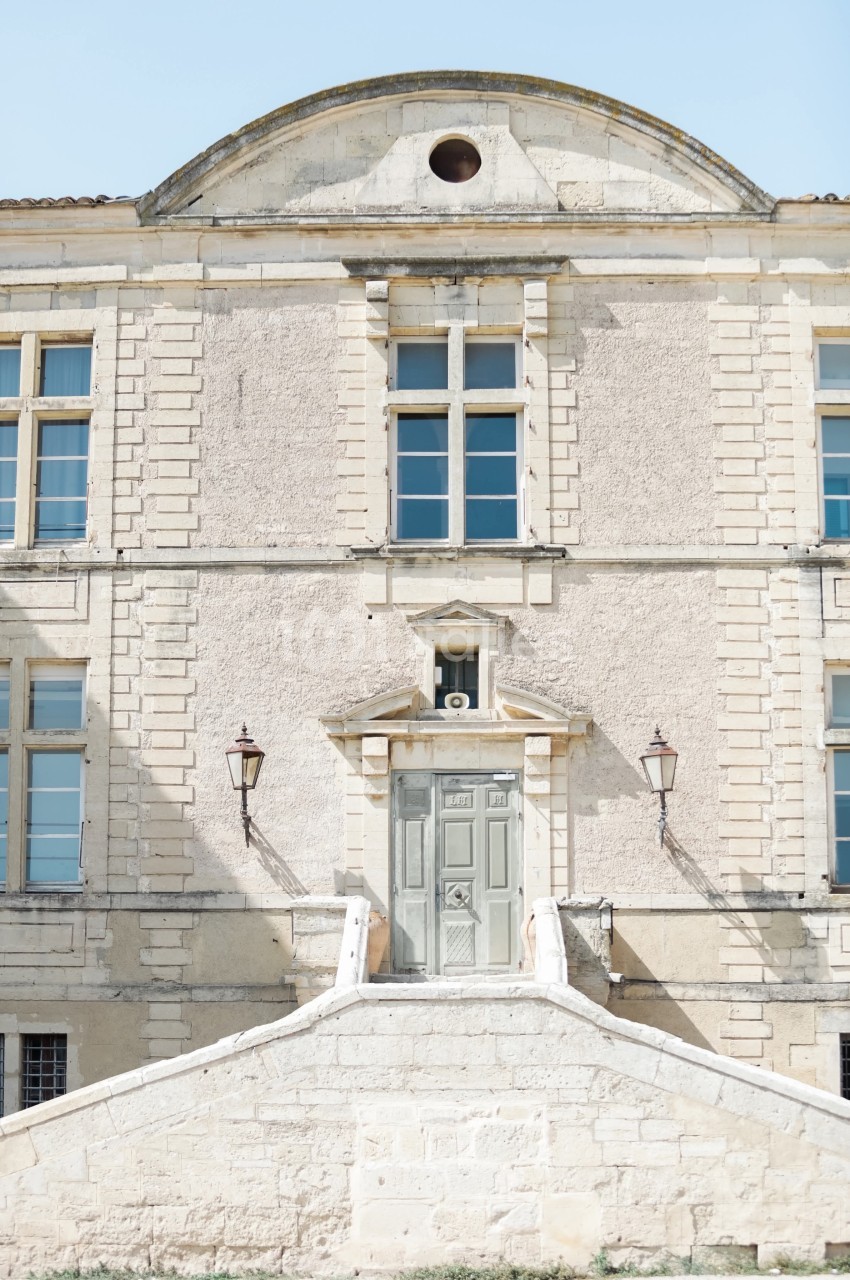 Façade d'un bâtiment ancien en pierre avec une porte centrale, des fenêtres symétriques et deux lanternes murales.