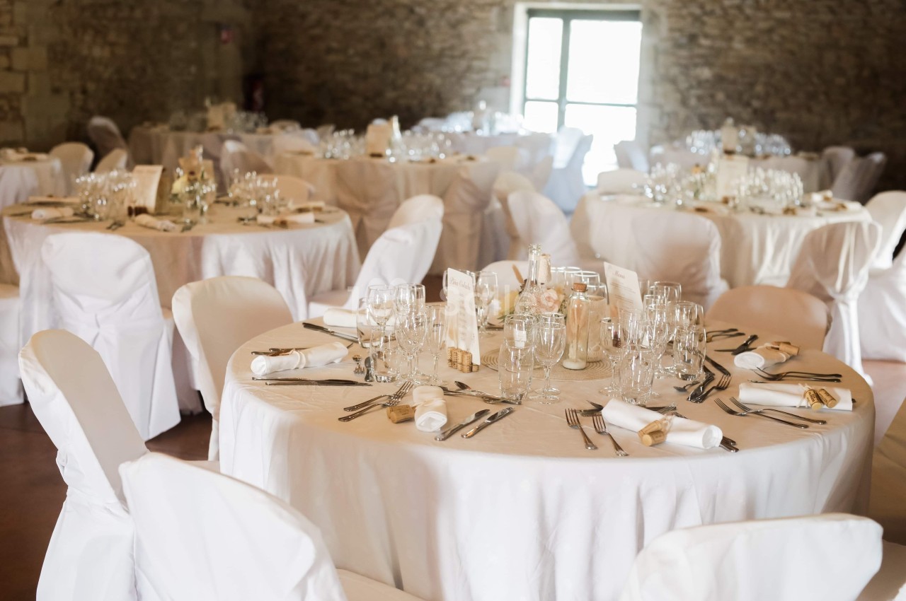 Salle de réception décorée avec des tables rondes couvertes de nappes blanches, dressées pour un événement.