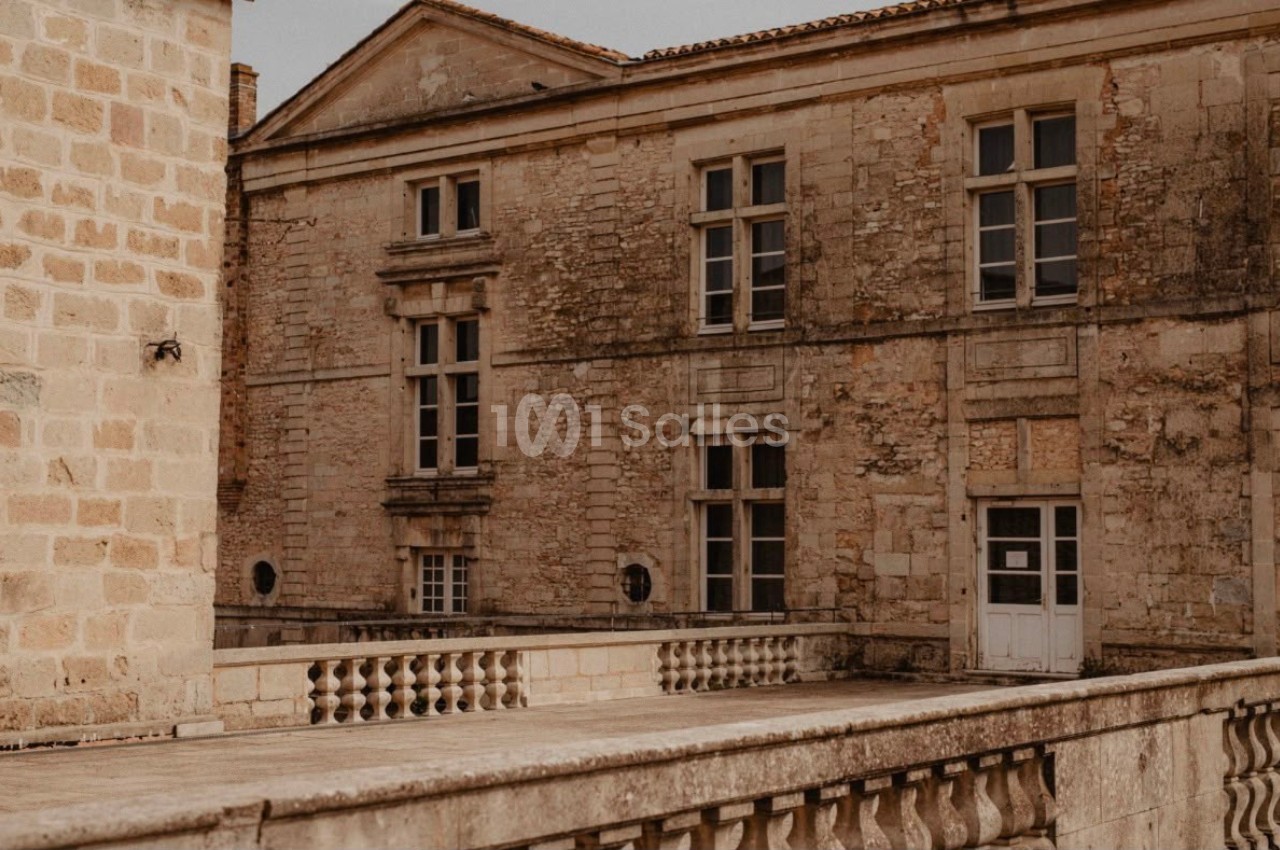 Façade en pierre d'un bâtiment ancien avec fenêtres à croisillons, vue depuis une balustrade en pierre.