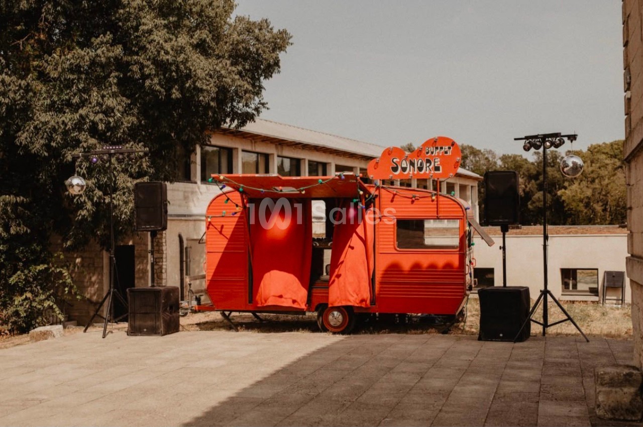 Caravane rouge aménagée en scène sonore, entourée de haut-parleurs, installée en extérieur près de bâtiments.