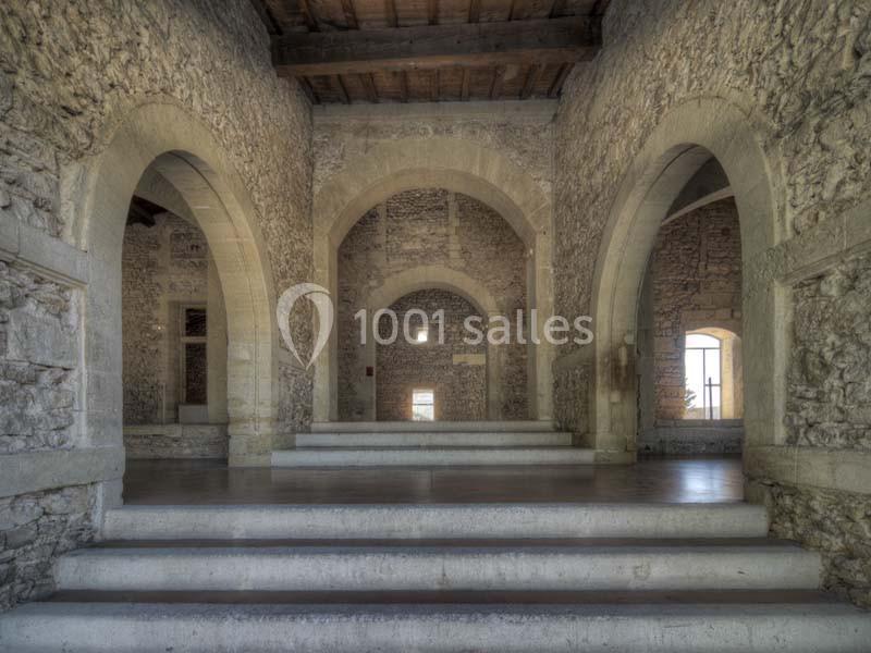 Intérieur d'un bâtiment en pierre avec des arches, des murs texturés et un plafond en bois.