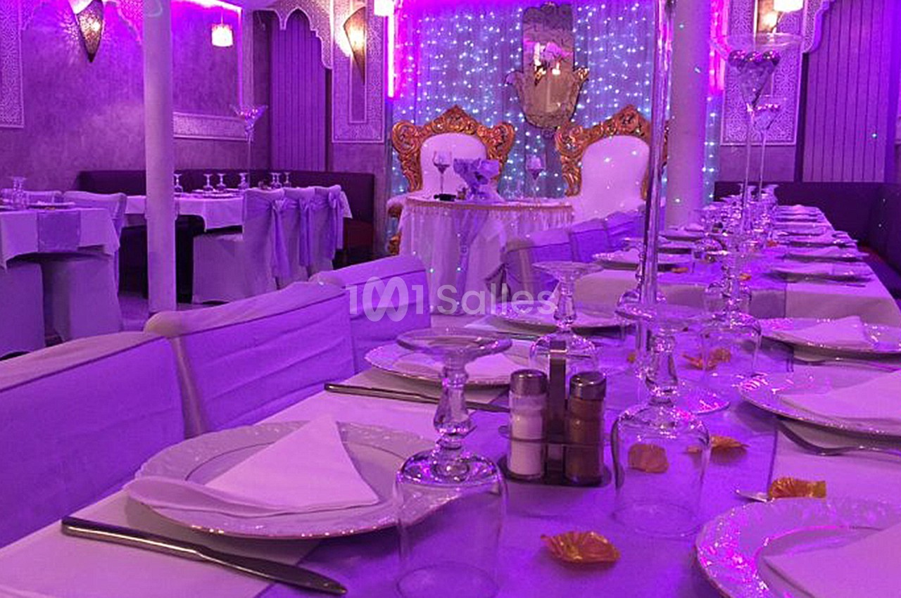Salle de réception décorée avec des tons violets, tables dressées avec vaisselle élégante et chaises couvertes.