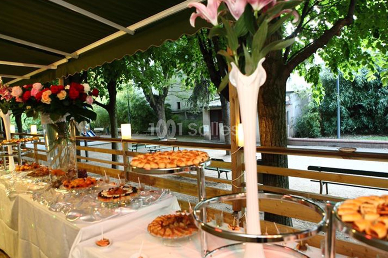 Buffet en extérieur sous un auvent, avec des fleurs et des arbres en arrière-plan.