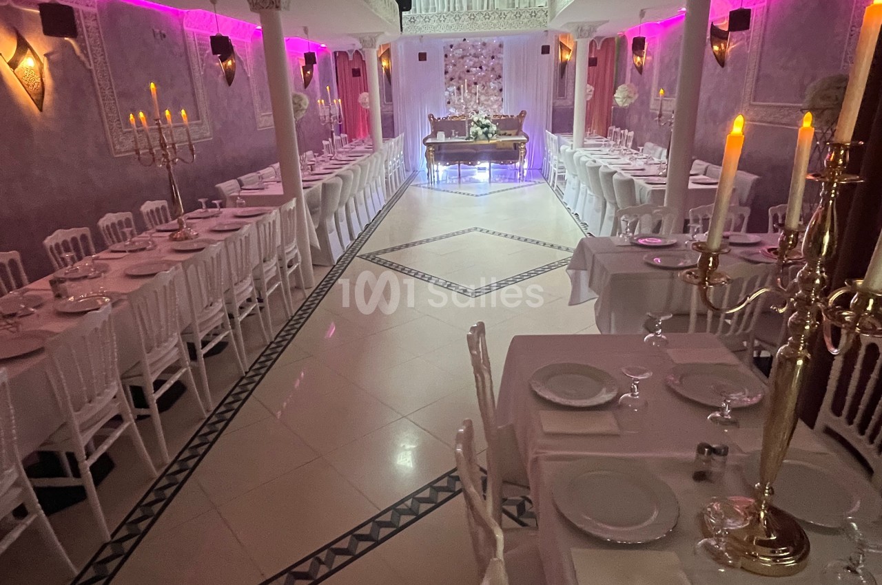 Salle de réception élégante avec tables dressées, chandeliers dorés et éclairage rose tamisé.