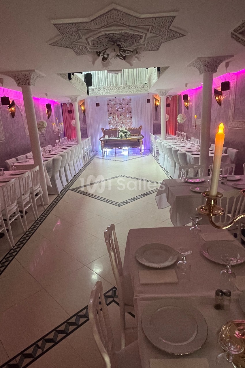 Salle de réception décorée avec des tables dressées, des chandeliers et un éclairage rose tamisé.