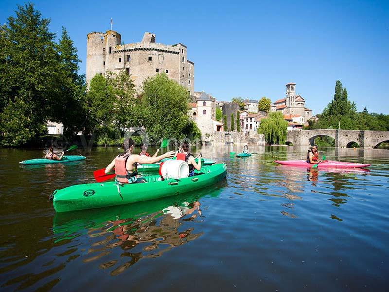 Personnes faisant du kayak sur une rivière calme, avec un château médiéval et un pont en arrière-plan.