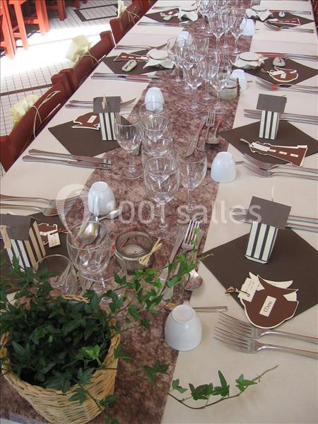 Table dressée pour un repas, avec nappes, serviettes brunes, verres, couverts, décorations et un panier de lierre.