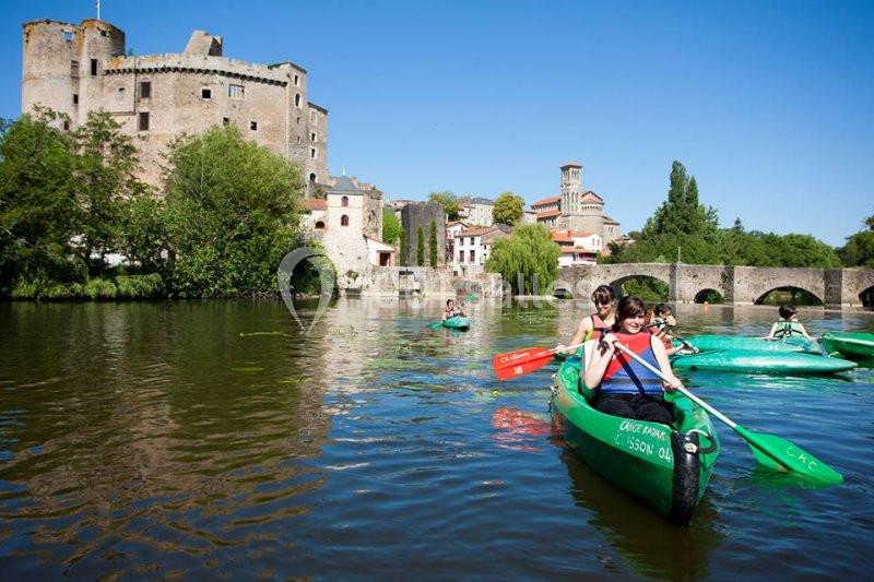Des personnes pagaient en canoë sur une rivière, avec un château médiéval et un pont en arrière-plan.