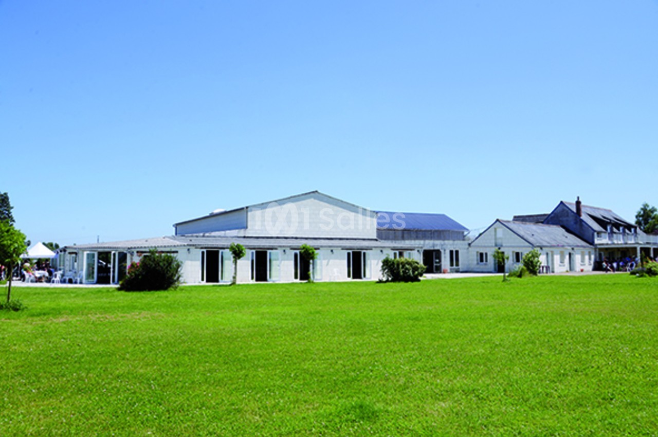 Bâtiment blanc moderne entouré d'une pelouse verte sous un ciel bleu dégagé.