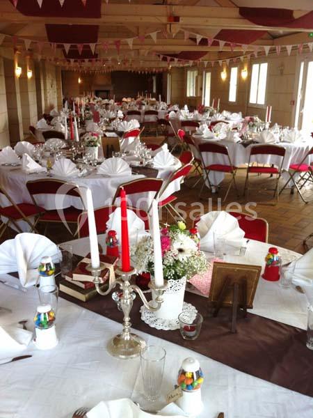 Salle décorée pour un événement avec tables dressées, nappes blanches, pliages de serviettes et chandeliers.