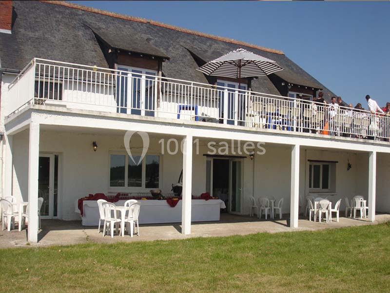 Façade d'une maison à deux étages avec terrasse, parasol, tables et chaises, donnant sur une pelouse.