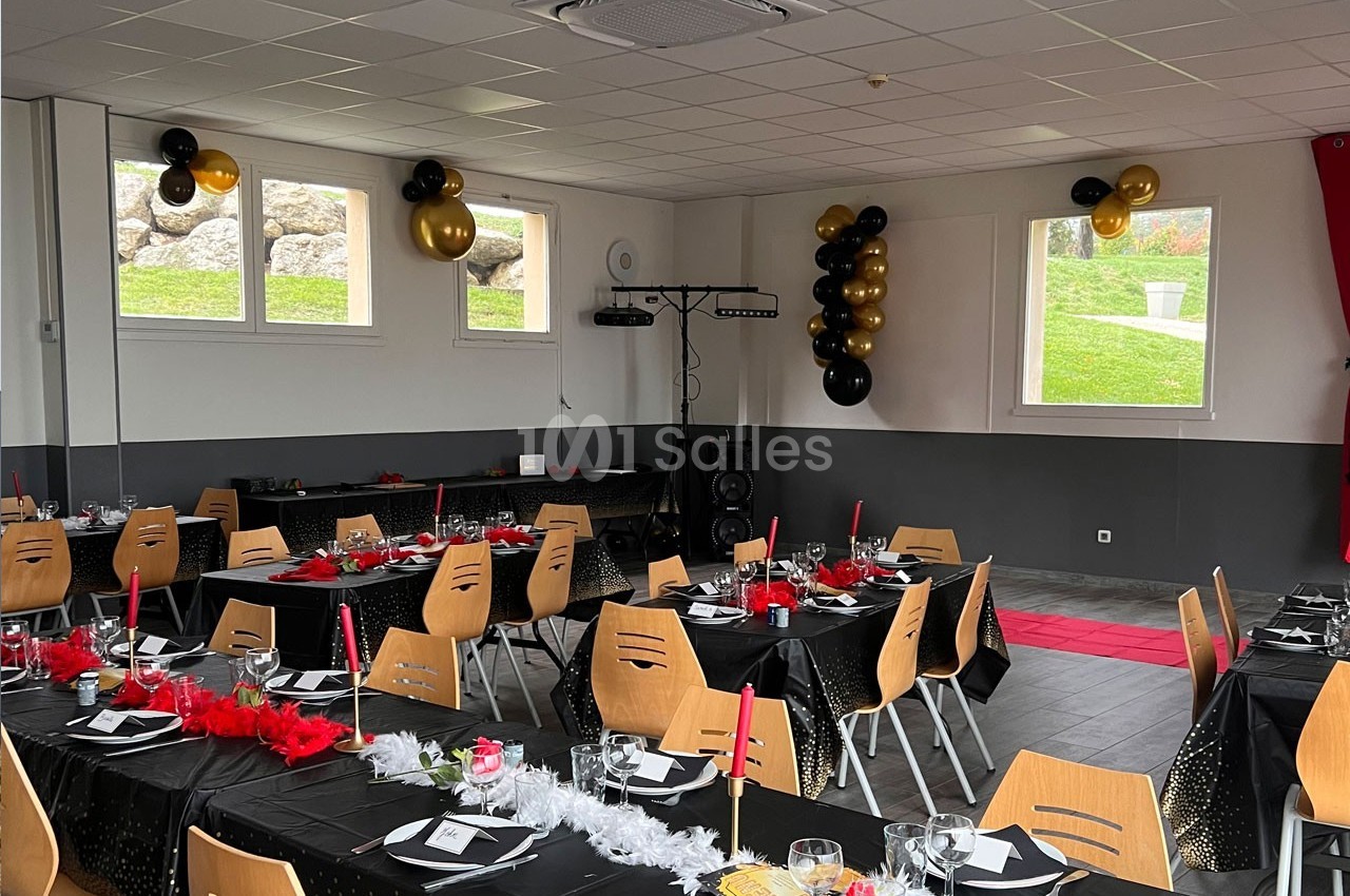 Salle décorée pour un événement avec tables dressées, nappes noires, bougies rouges et ballons noirs et dorés.