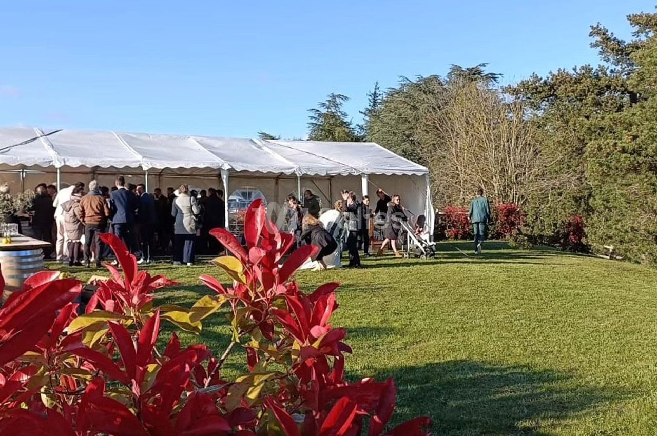 Groupe de personnes rassemblées près d'une tente blanche dans un jardin verdoyant par une journée ensoleillée.